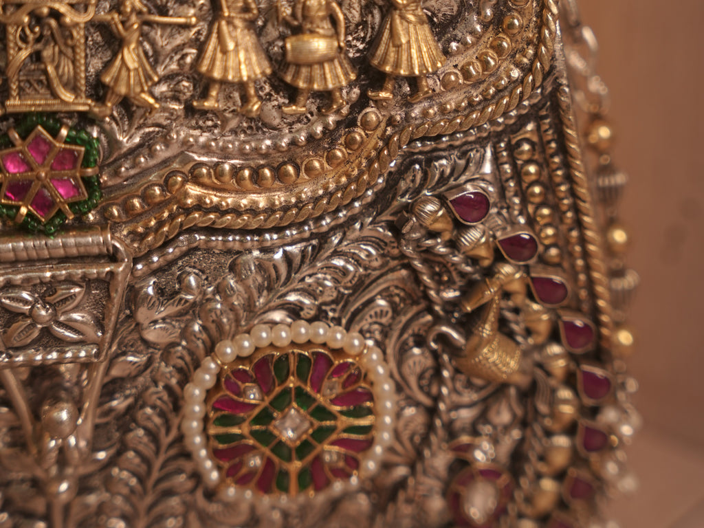 Detail of a meena work medallion ringed with small white beads, beside the chased silver foliage.