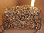 The silver baraat purse standing upright, bangle handles raised and the floral clasp closed.