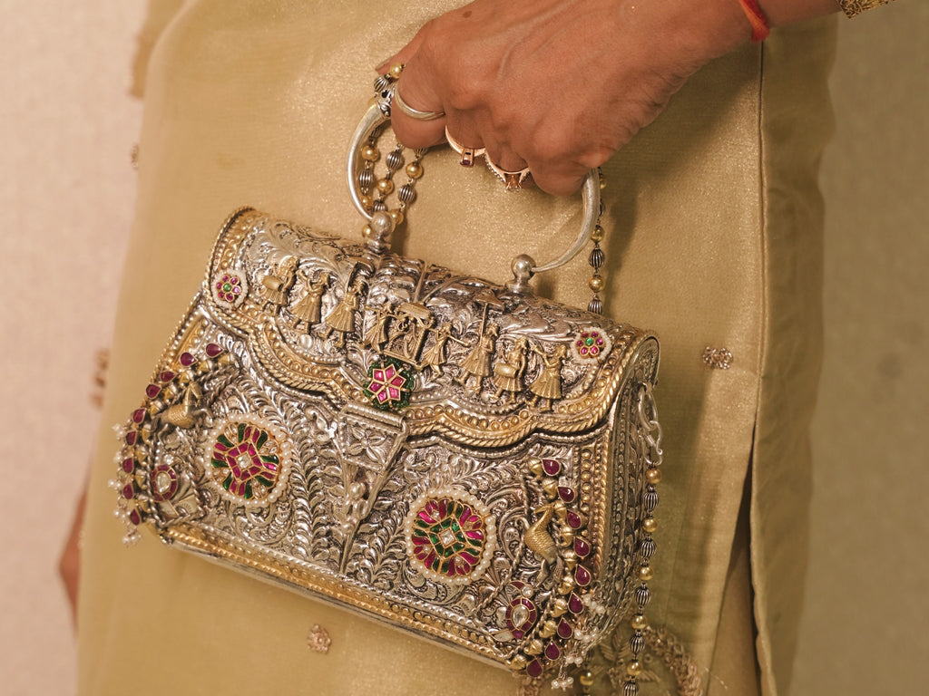 The silver purse carried in hand by its bangle handles against a gold outfit.