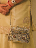 The purse worn on the shoulder by its bead chain, hanging against a gold outfit.