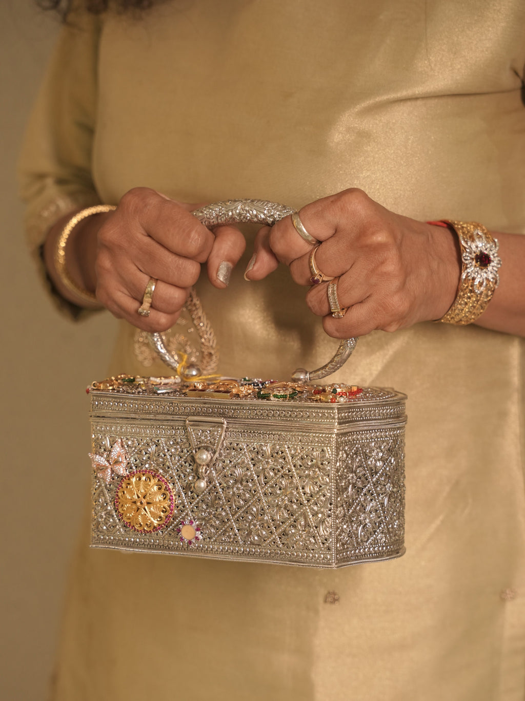 The silver filigree box purse held by its oval handle, charm studded lid facing forward.