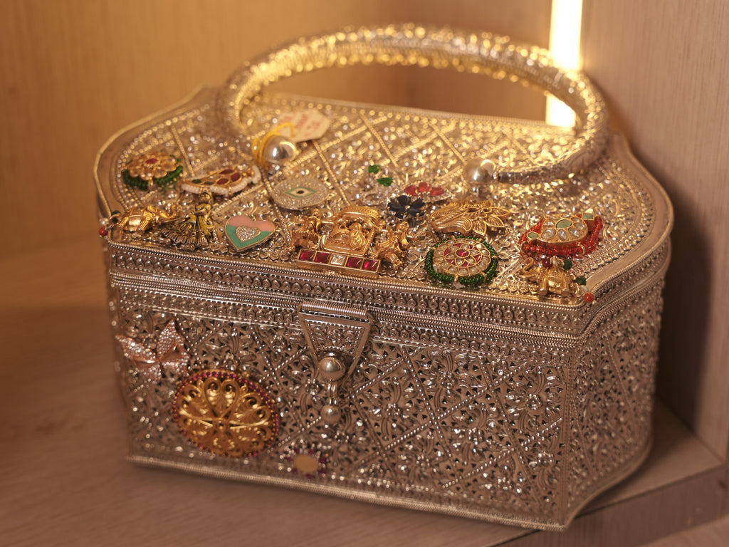 The filigree vanity box purse on a shelf, showing the scalloped lid covered with gold-tone and stone set charms.