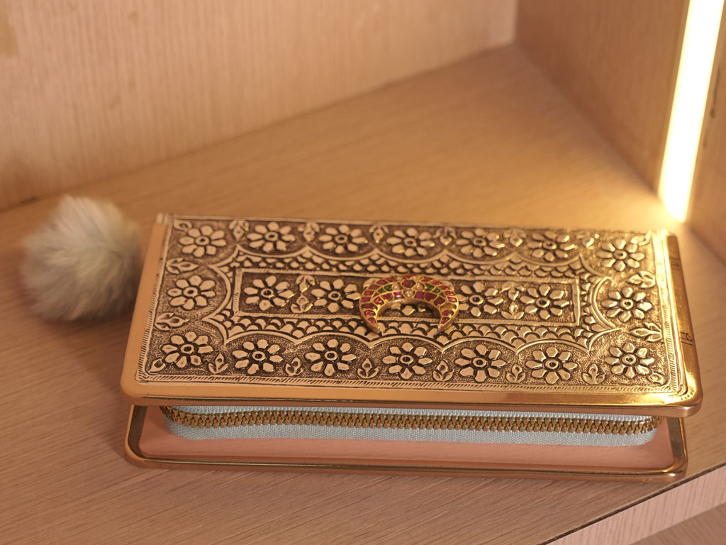 The oxidised silver clutch wallet lying flat, showing the meena crescent panel and the fur pom pull on the zip.