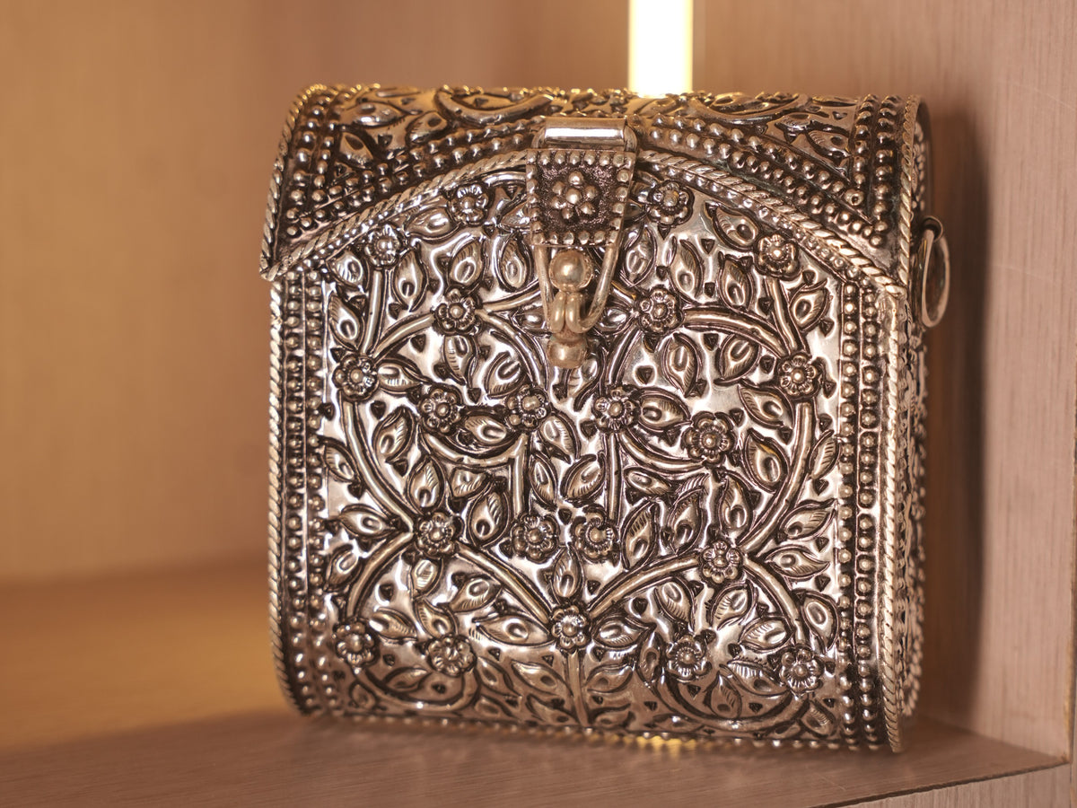 Angled view of the oxidised box bag, showing the curved flap, hook clasp and side ring for a sling chain.