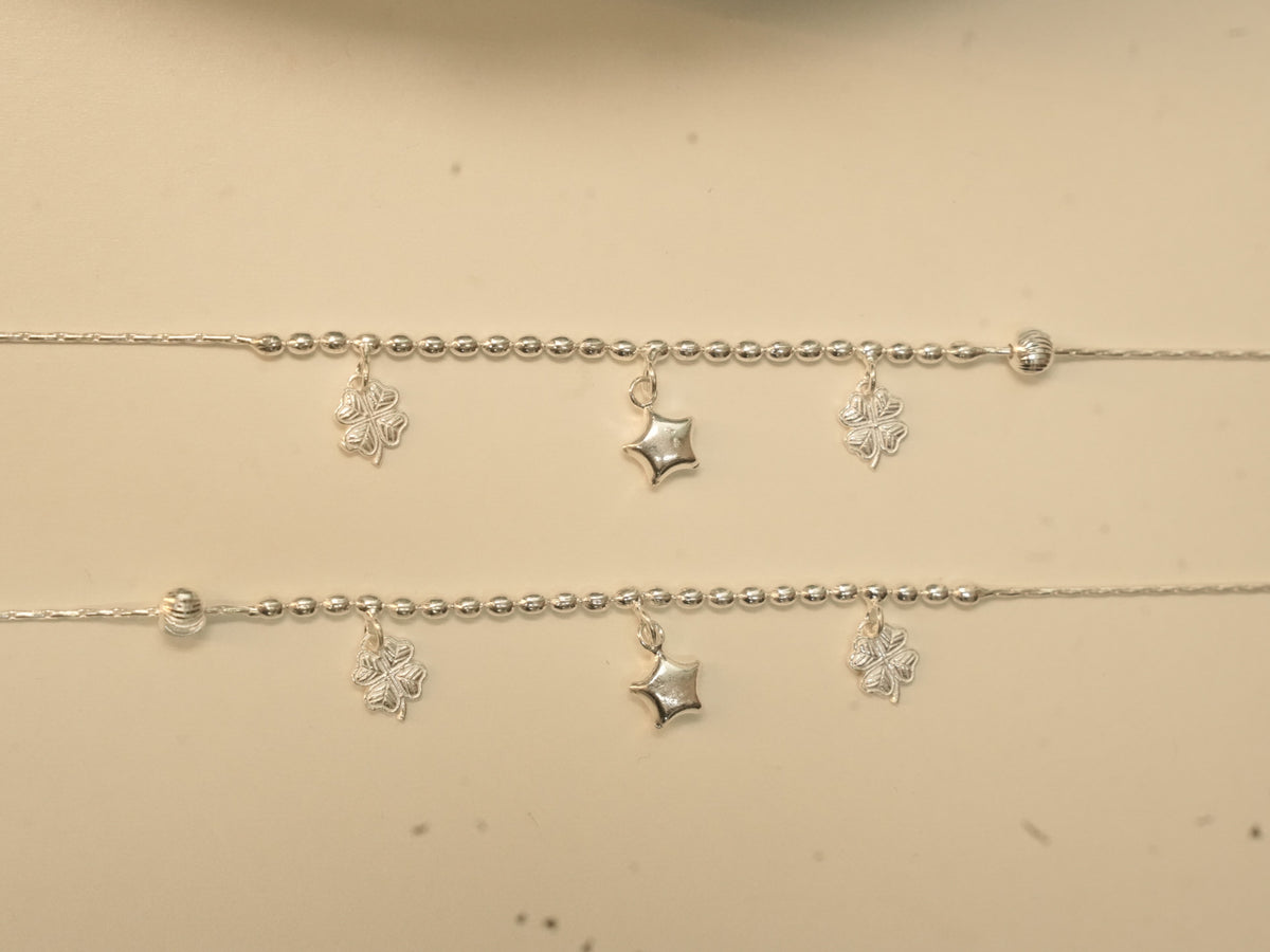 Close view of the clover and star charms hanging below the rice beads on the silver payal.