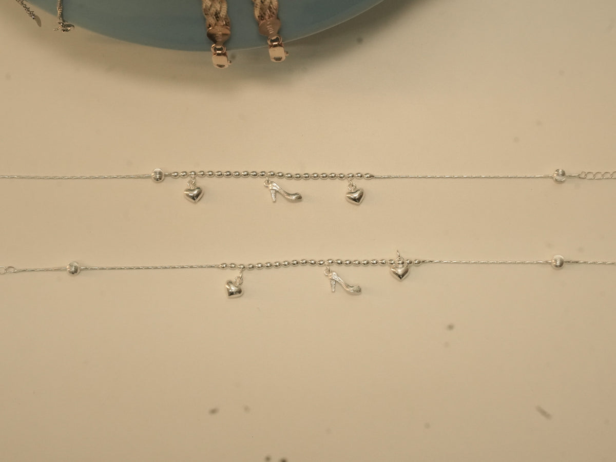 The pair of heart and heel payal laid out to show the charms and the extender chain.