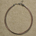 Multi-strand anklet of fine textured silver and rose gold-tone strands with a lobster clasp and extender chain, laid flat on beige fabric.