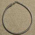 Sterling silver anklet with a twisted rope texture and slender clasp, photographed on beige woven fabric.