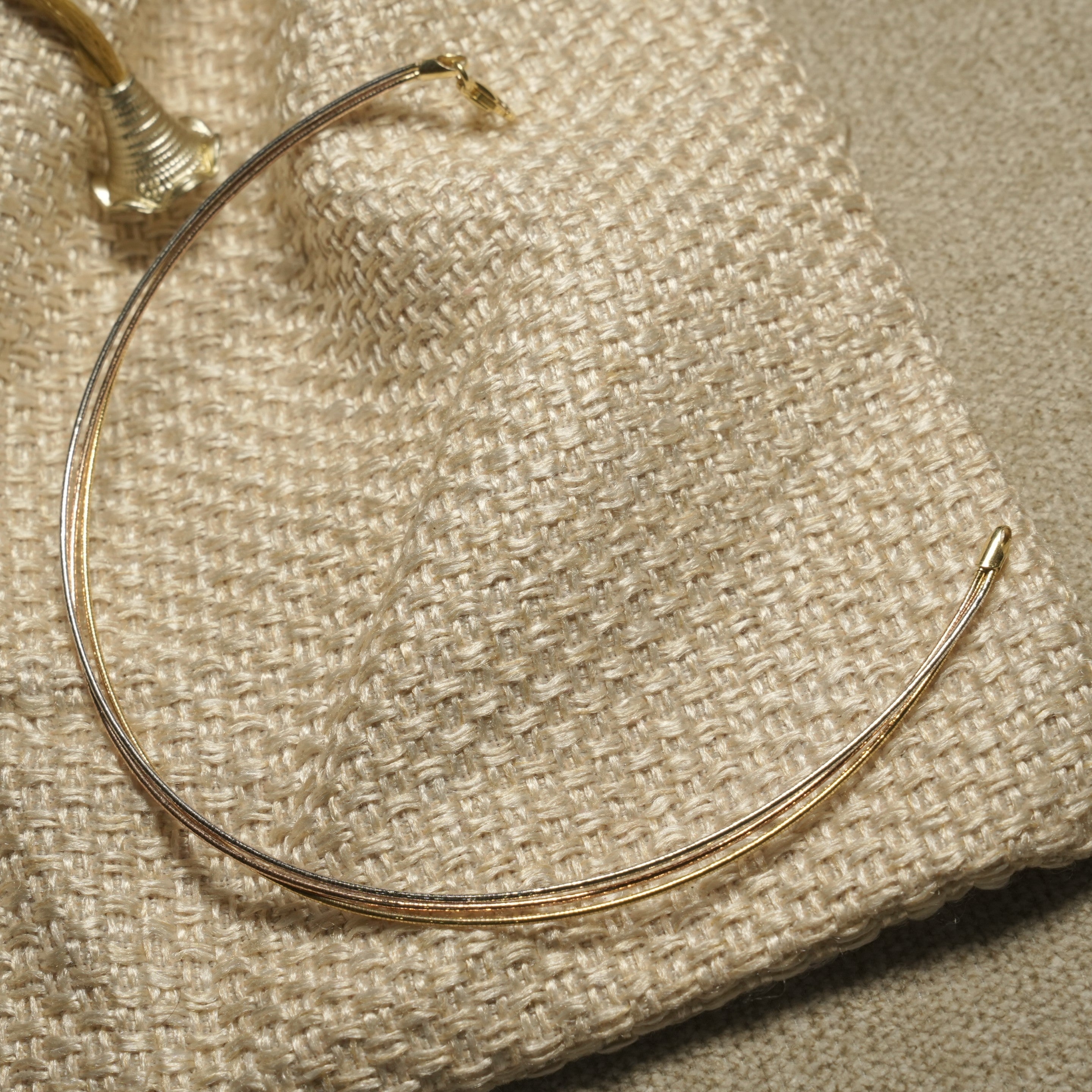 Slim mixed-tone sterling silver anklet with gold-tone clasp, arranged in a curve on ivory woven fabric.