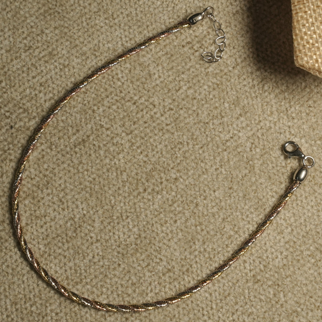 Twisted tri-tone sterling silver anklet with lobster clasp and extender chain laid in a loop on beige fabric.