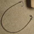 Twisted tri-tone sterling silver anklet with lobster clasp and extender chain laid in a loop on beige fabric.