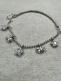 Sterling silver anklet on grey felt, with star and butterfly charms hanging from the ball chain and the engraved bar curving away at the left.