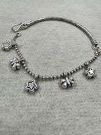 Sterling silver anklet on grey felt, with star and butterfly charms hanging from the ball chain and the engraved bar curving away at the left.