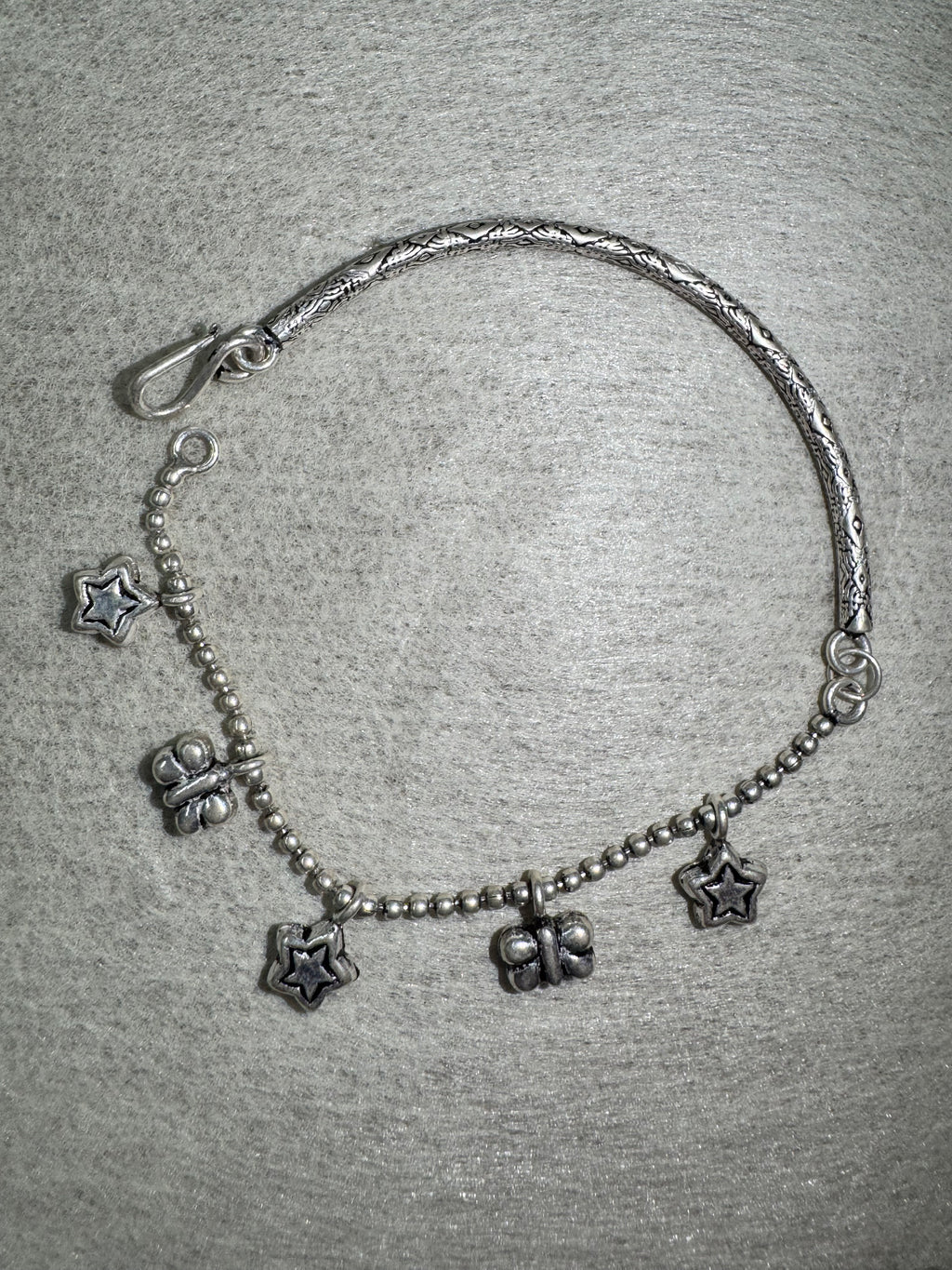 The sterling silver anklet laid in an open curve, showing the S-hook closure and the alternating star and butterfly charms.