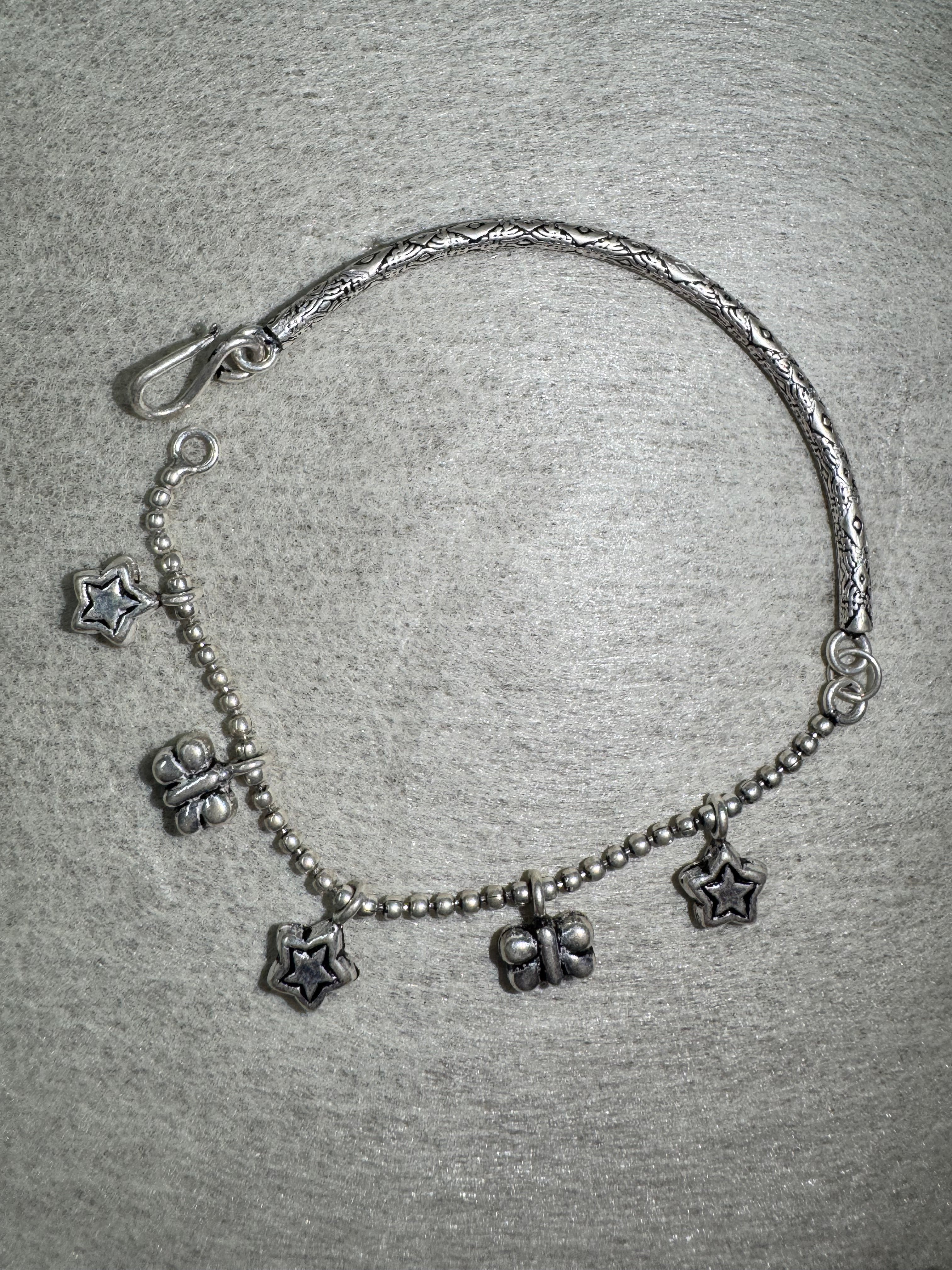 The sterling silver anklet laid in an open curve, showing the S-hook closure and the alternating star and butterfly charms.