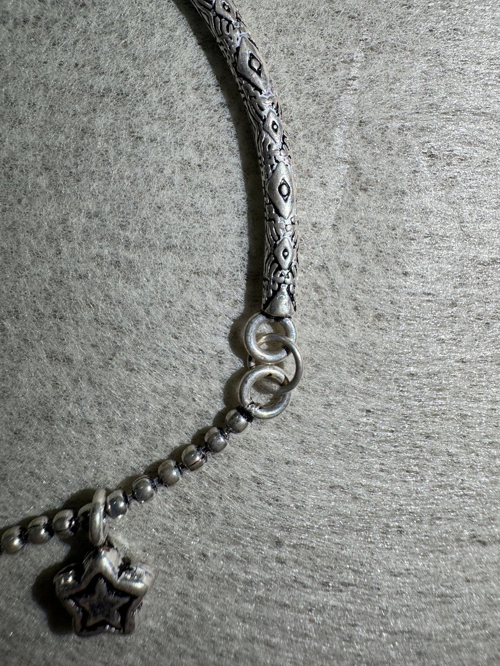 Close view of the engraved pattern on the anklet's sterling silver bar and the two jump rings joining it to the ball chain.