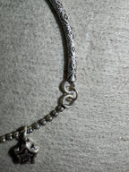 Close view of the engraved pattern on the anklet's sterling silver bar and the two jump rings joining it to the ball chain.