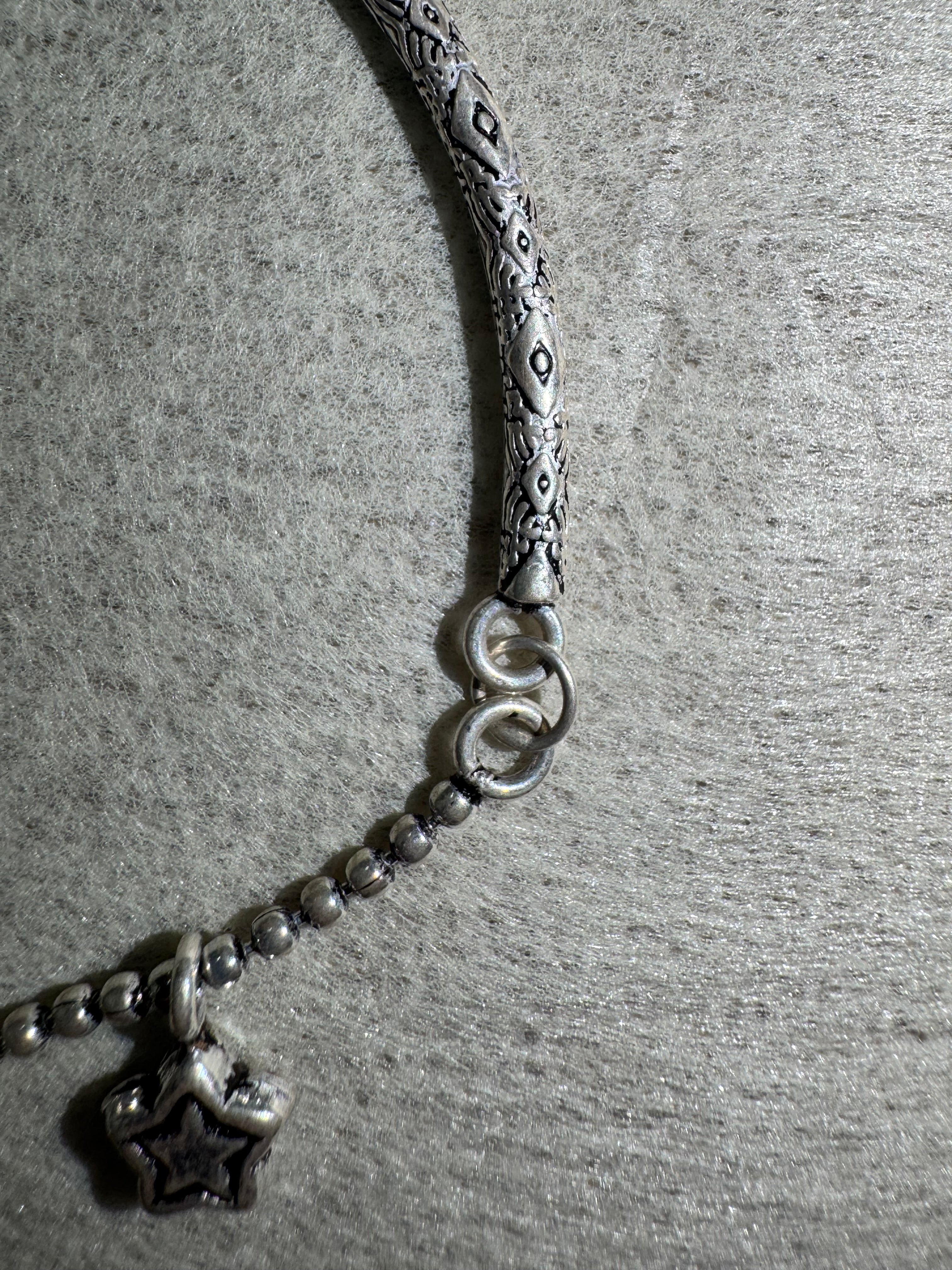 Close view of the engraved pattern on the anklet's sterling silver bar and the two jump rings joining it to the ball chain.