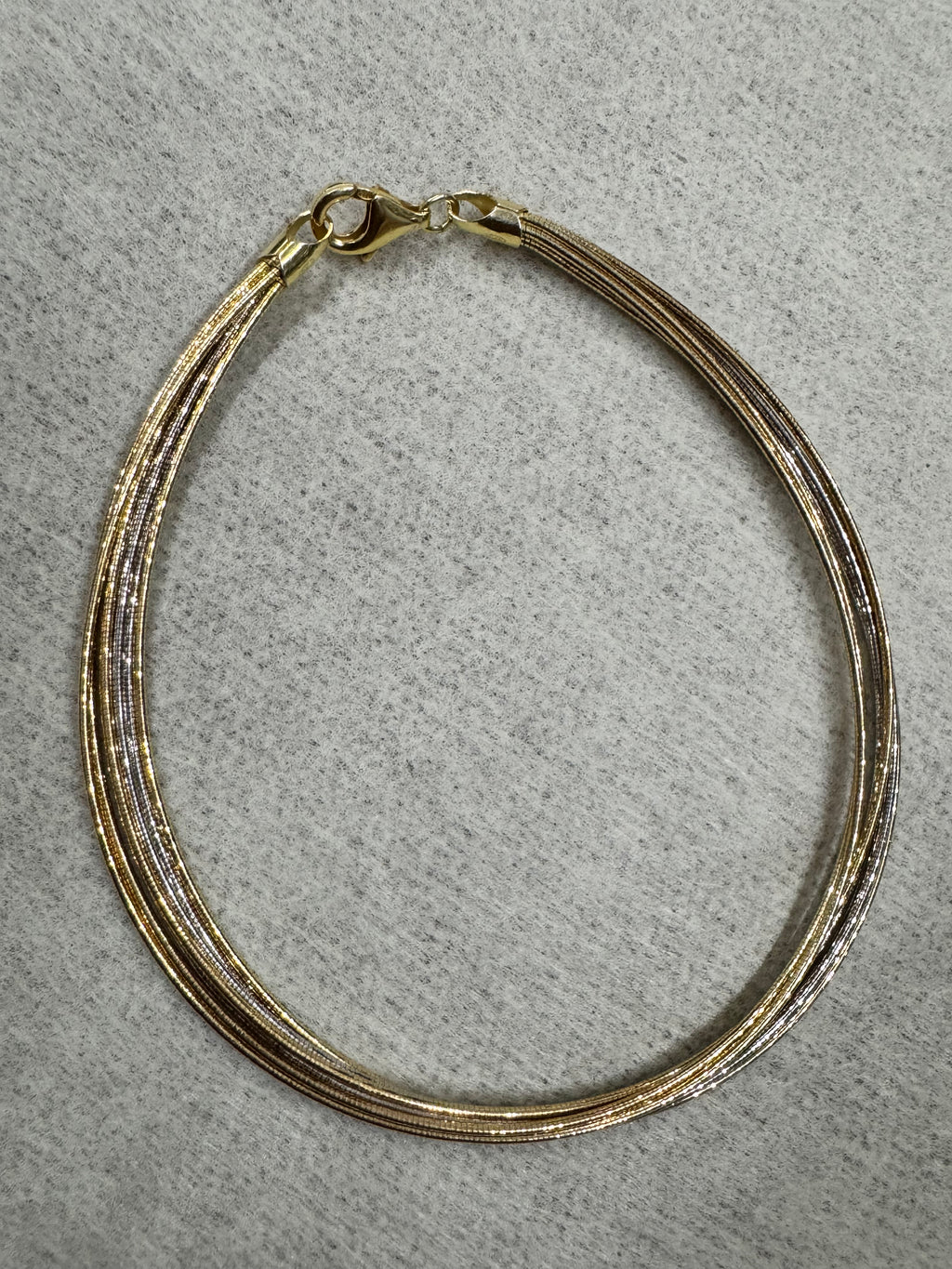 Two-tone sterling silver anklet of fine snake chains laid in a loop on grey felt, with the lobster clasp at the left.