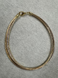 Two-tone sterling silver anklet of fine snake chains laid in a loop on grey felt, with the lobster clasp at the left.