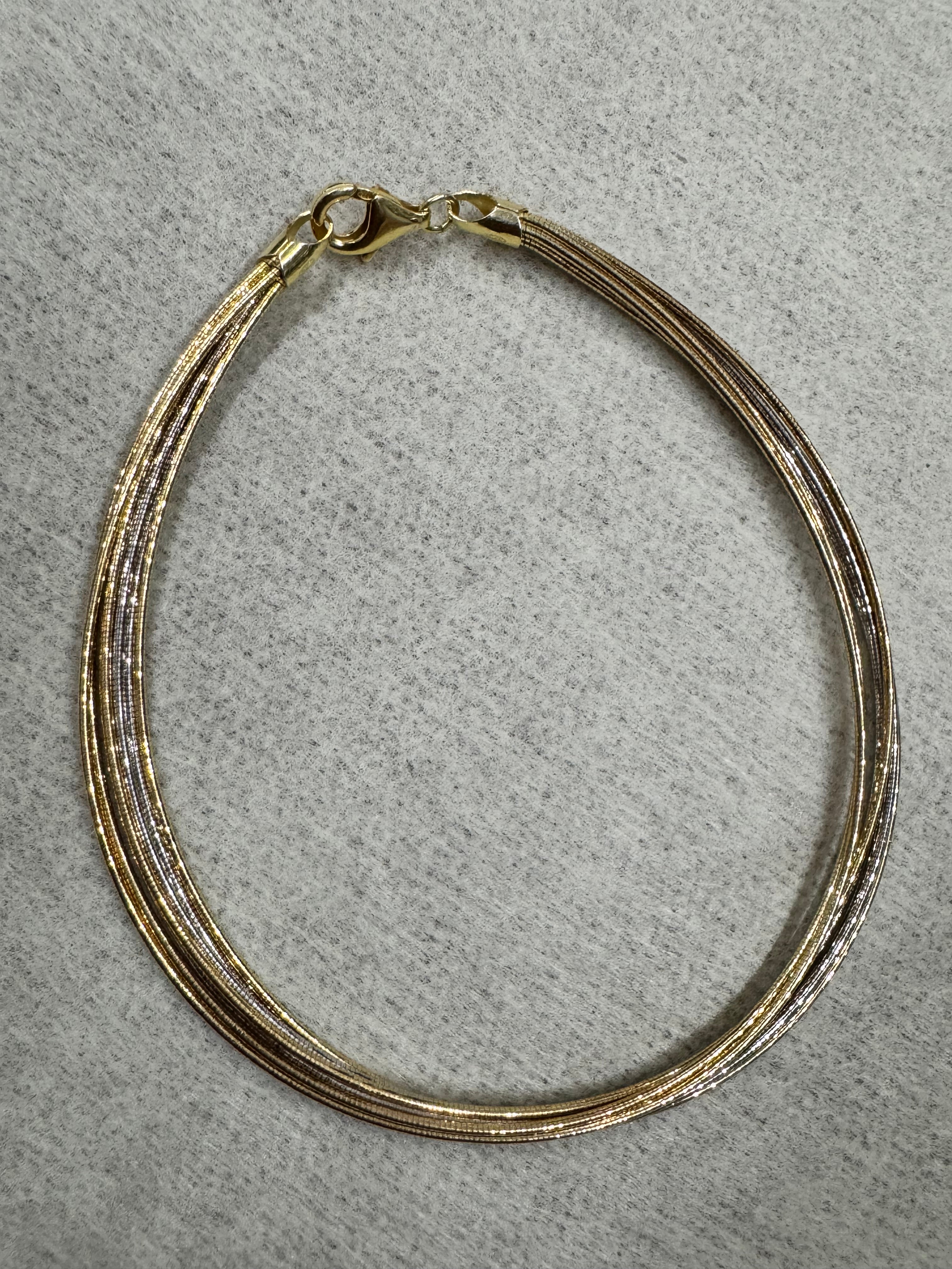 Two-tone sterling silver anklet of fine snake chains laid in a loop on grey felt, with the lobster clasp at the left.