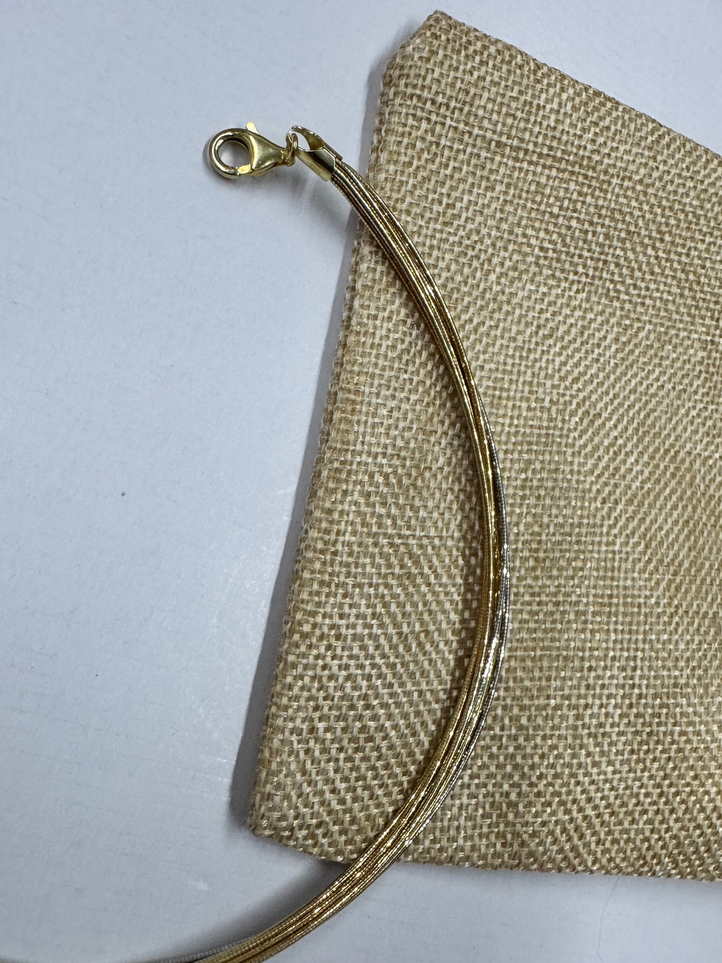 The clasp end of the two-tone sterling silver snake chain anklet resting across a jute pouch.