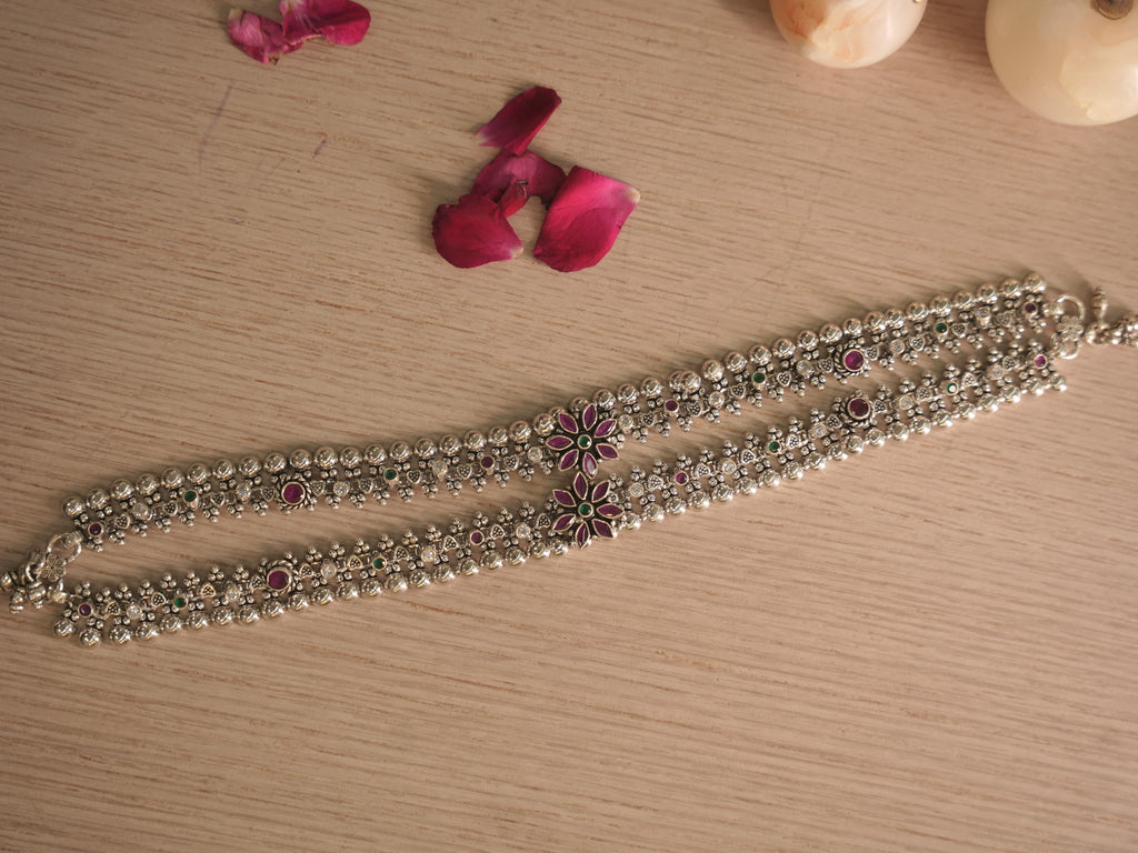 Pair of silver payal with pink and green stone flower clusters, laid side by side on a pale wooden surface with rose petals.