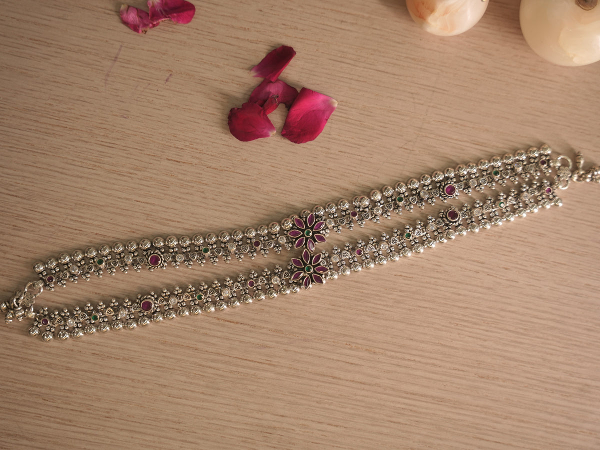 Pair of silver payal with pink and green stone flower clusters, laid side by side on a pale wooden surface with rose petals.