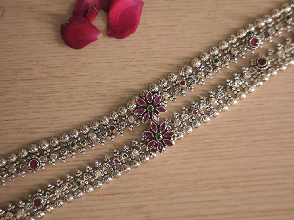Close view of the two silver payal, showing the woven band and the flower clusters with deep pink petal shaped stones.