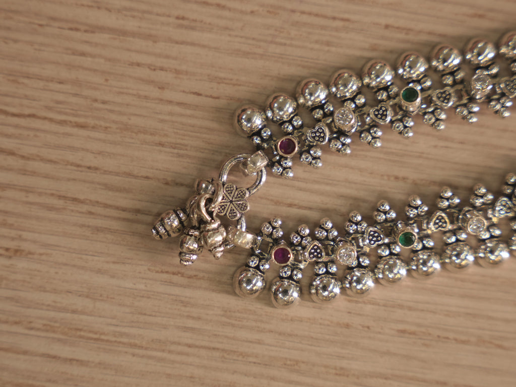 Clasp end of the silver payal, with heart and shell shaped charms hanging beside the ring closure.
