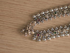 Clasp end of the silver payal, with heart and shell shaped charms hanging beside the ring closure.