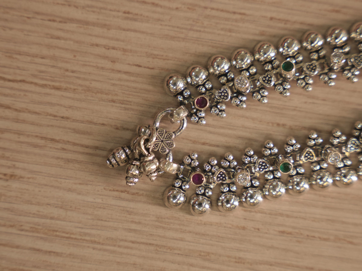 Clasp end of the silver payal, with heart and shell shaped charms hanging beside the ring closure.
