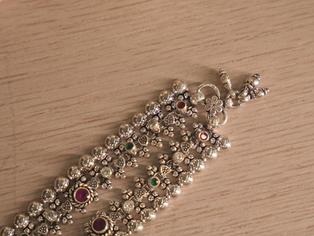 Sterling silver payal arranged in a curve, showing bezel set pink, green and colourless stones along the band.