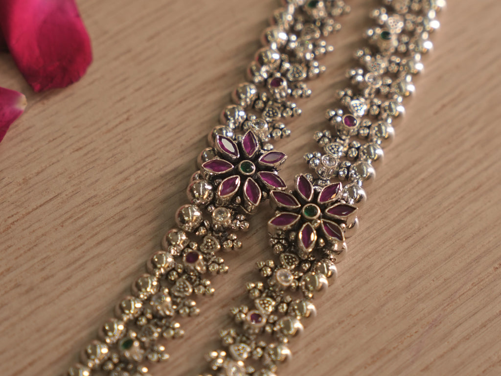 Angled close up of a flower cluster on the silver payal, with deep pink petal stones around a green centre.