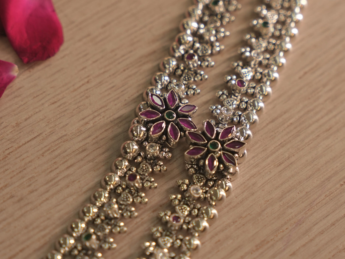 Angled close up of a flower cluster on the silver payal, with deep pink petal stones around a green centre.