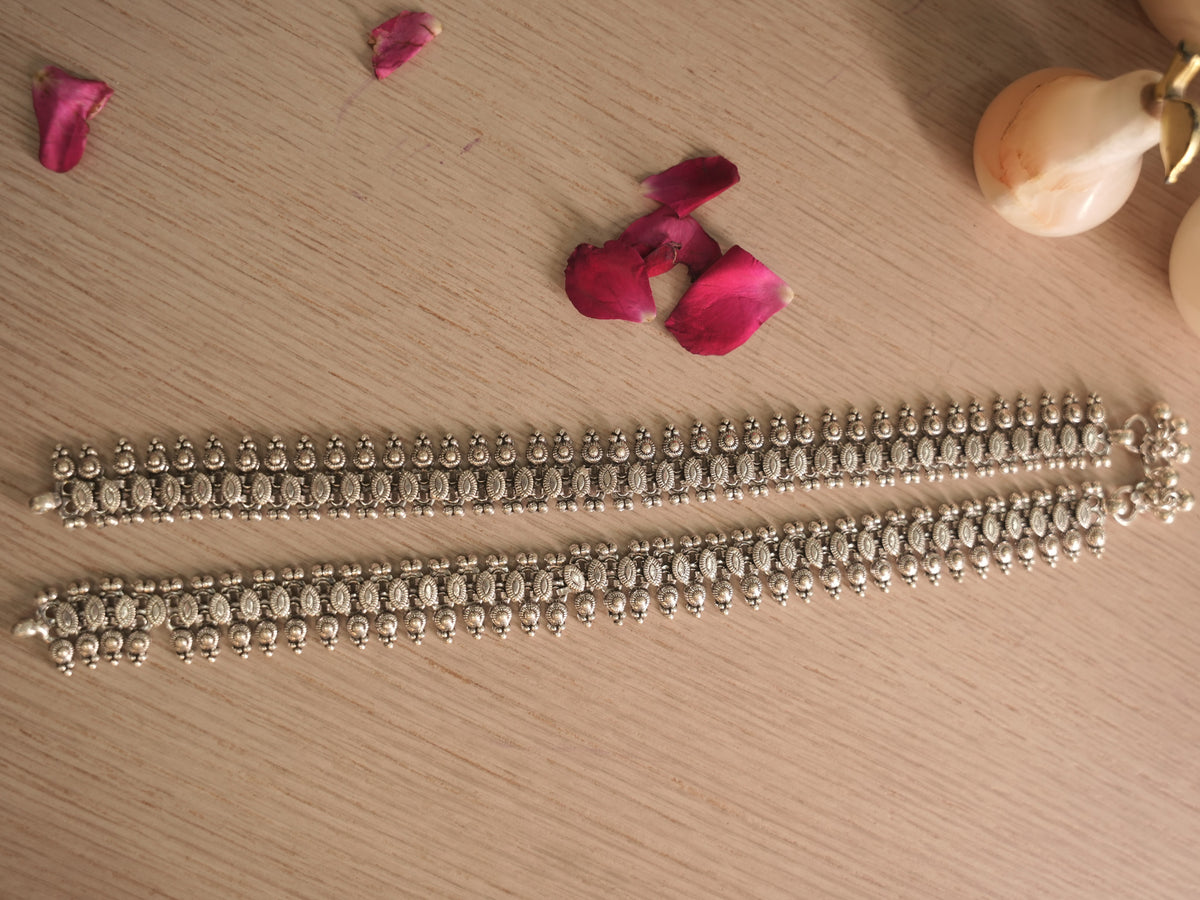 Pair of broad oxidised silver payal laid side by side, showing coin disc rows and textured marquise links.