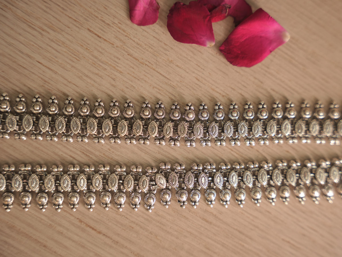 Close view of the oxidised silver payal panel, with stamped coin discs above a band of textured links and hanging domes.