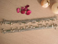Pair of broad oxidised silver payal with leaf shaped drops and ghungroos, laid out on a pale surface.