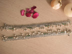 Pair of broad oxidised silver payal with leaf shaped drops and ghungroos, laid out on a pale surface.