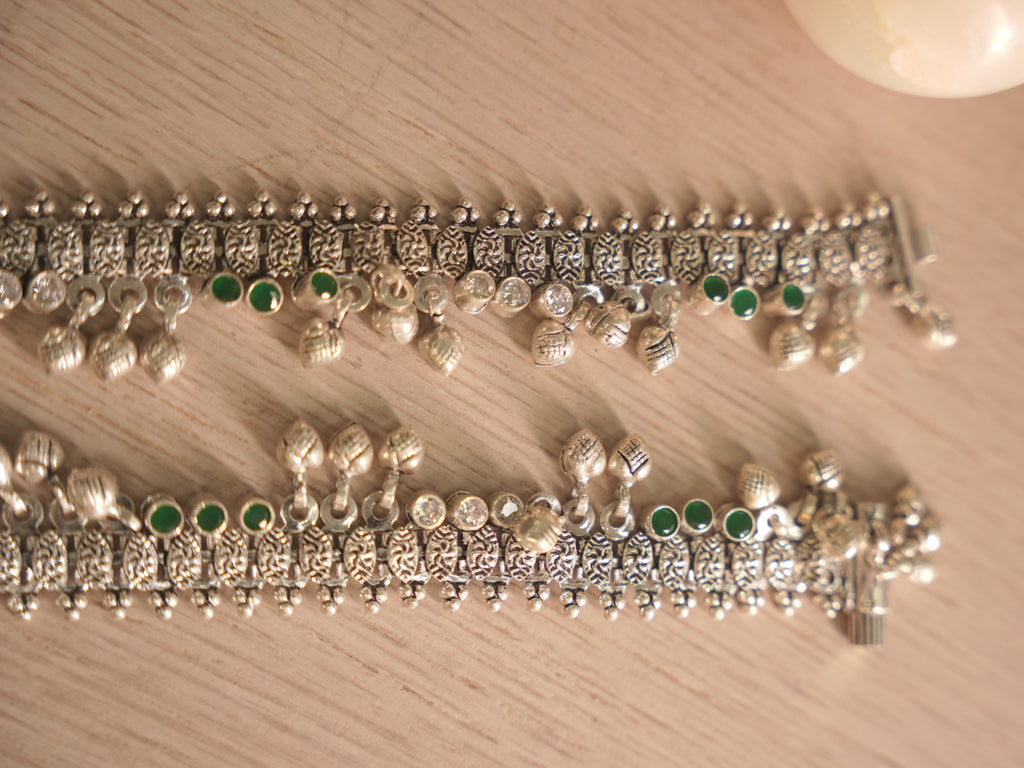 Both oxidised silver payal overlapping, showing the woven band and the spacing of green and colourless stones.