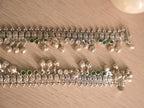Both oxidised silver payal overlapping, showing the woven band and the spacing of green and colourless stones.