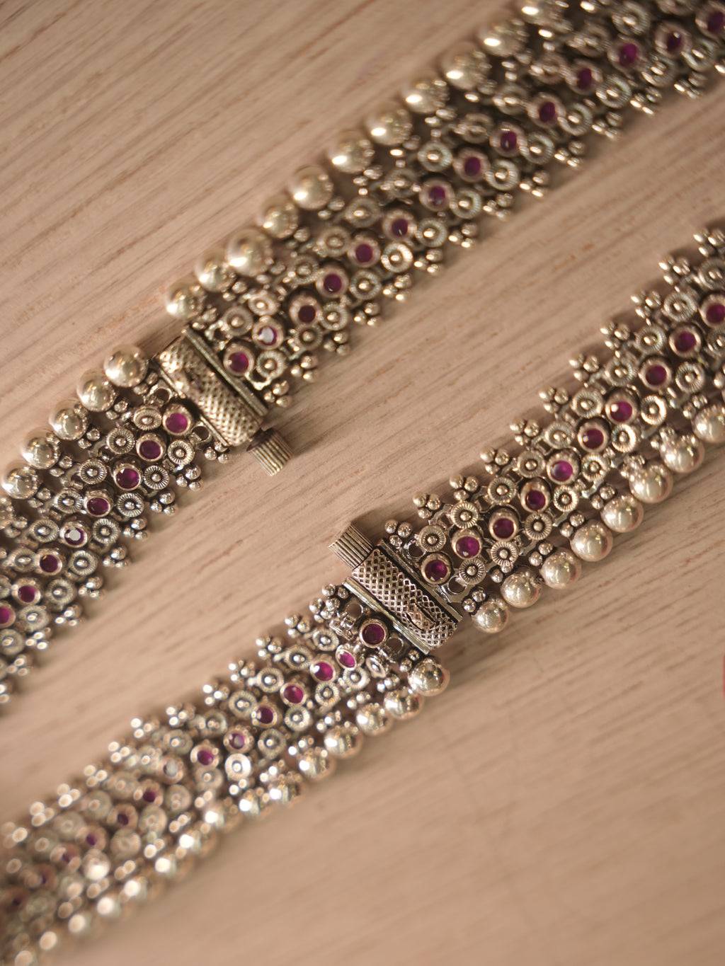 Pair of wide silver payal with rows of deep pink glass stones, laid flat on a pale background.