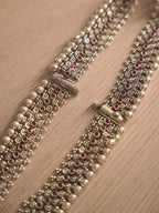 Upright view of a silver payal, showing the floral jaali band and pink glass stones along its centre.