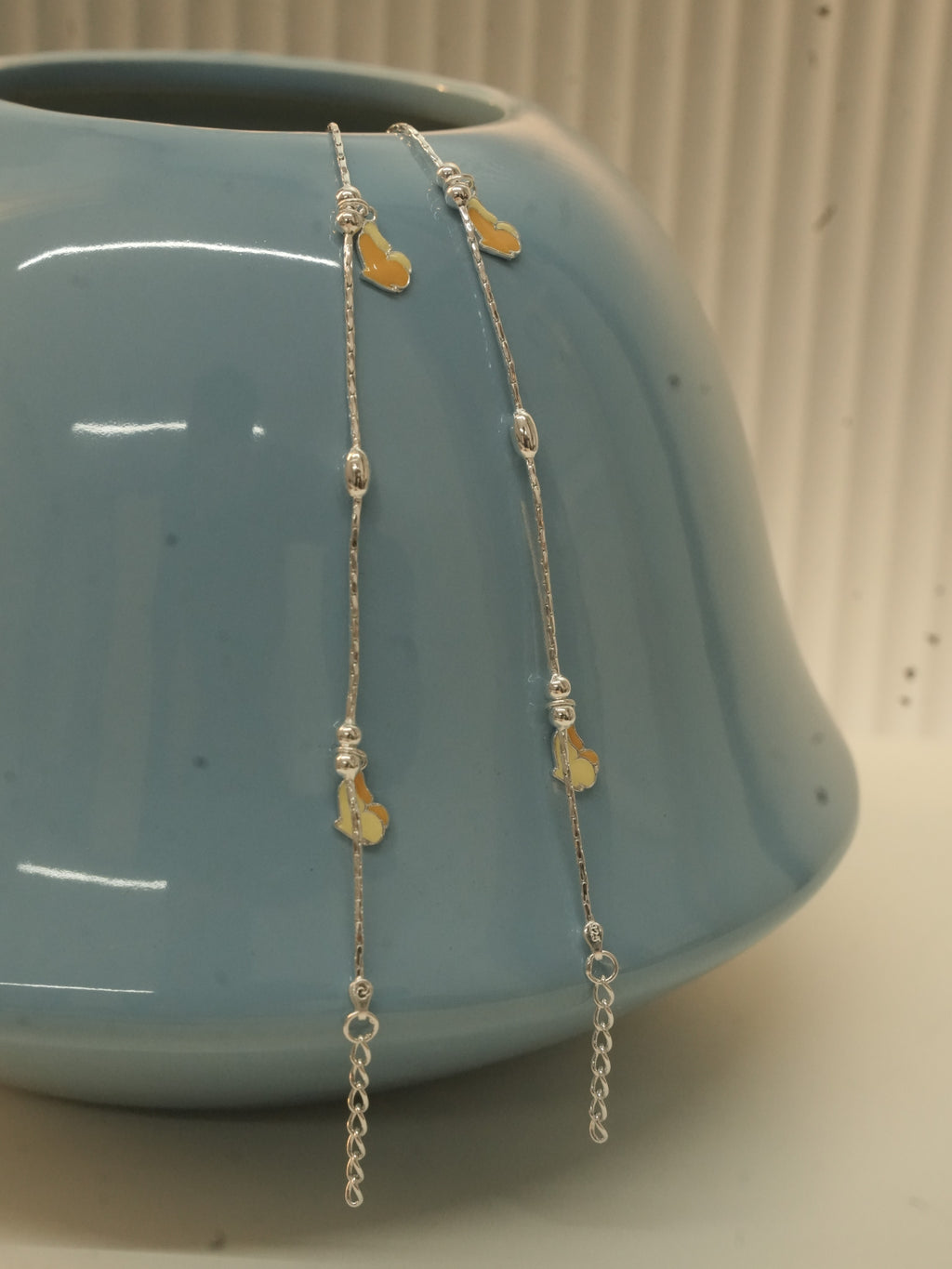 Pair of silver payal with yellow and orange enamel butterflies, draped over a blue ceramic vase.