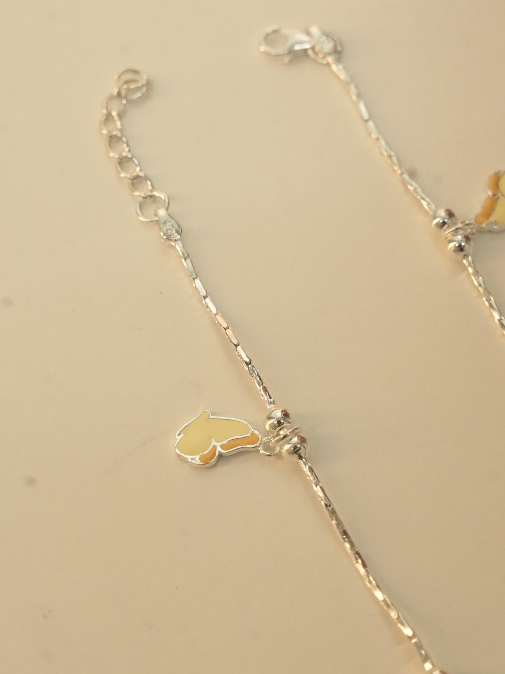 An enamel butterfly beside a bead cluster on the silver payal, with the lobster clasp and extender chain above.