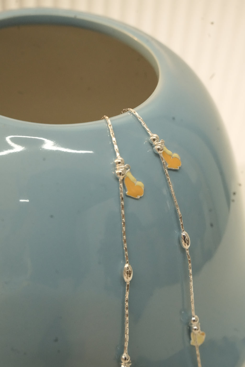 The butterfly payal hanging over the rim of a blue vase, showing the oval silver beads.