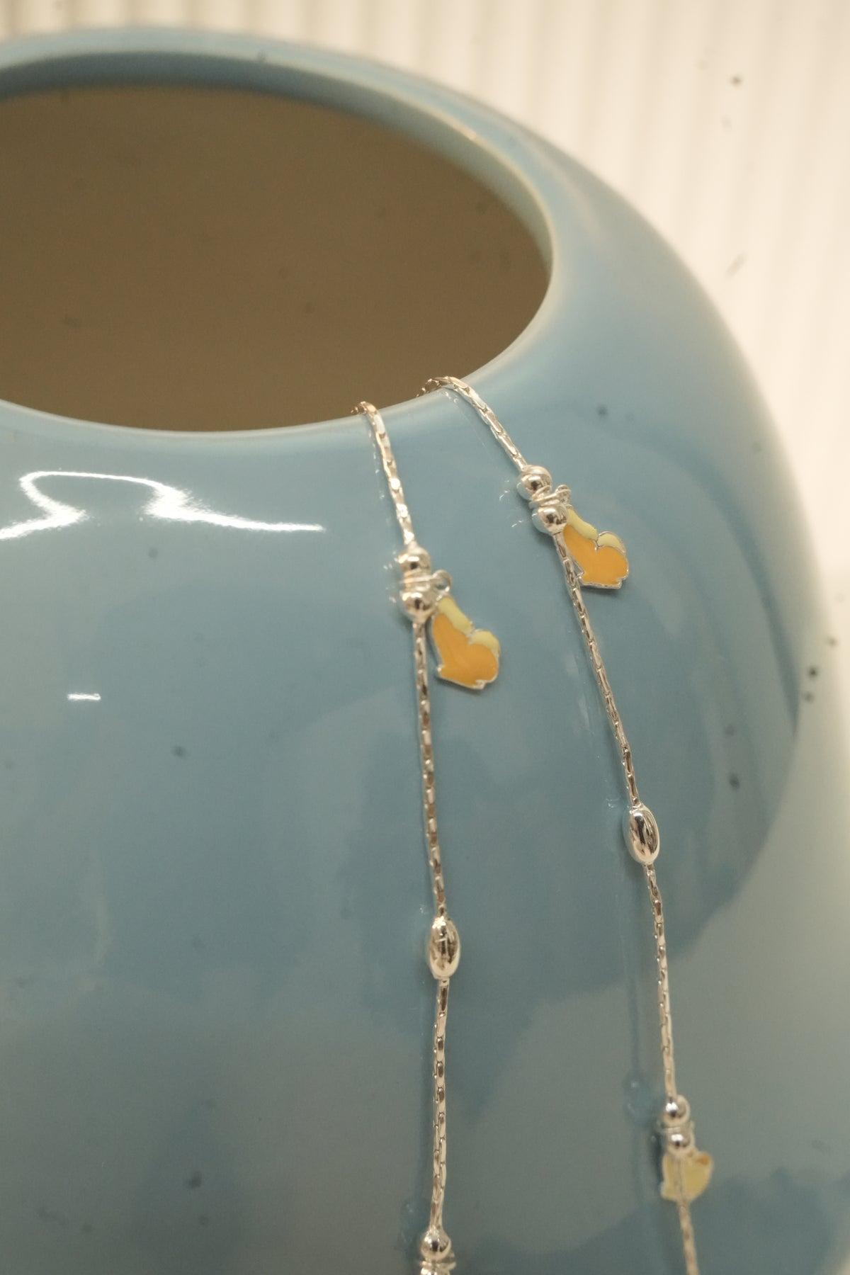 The butterfly payal hanging over the rim of a blue vase, showing the oval silver beads.