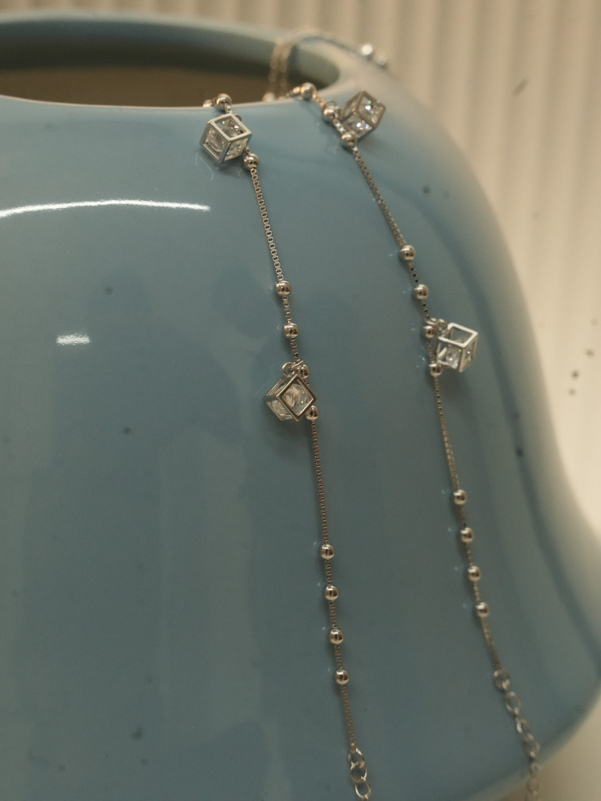 The cube charm payal draped over a blue ceramic vase.