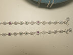 The pair of oval halo payal laid out full length, showing pink and green stone links among the colourless ones.