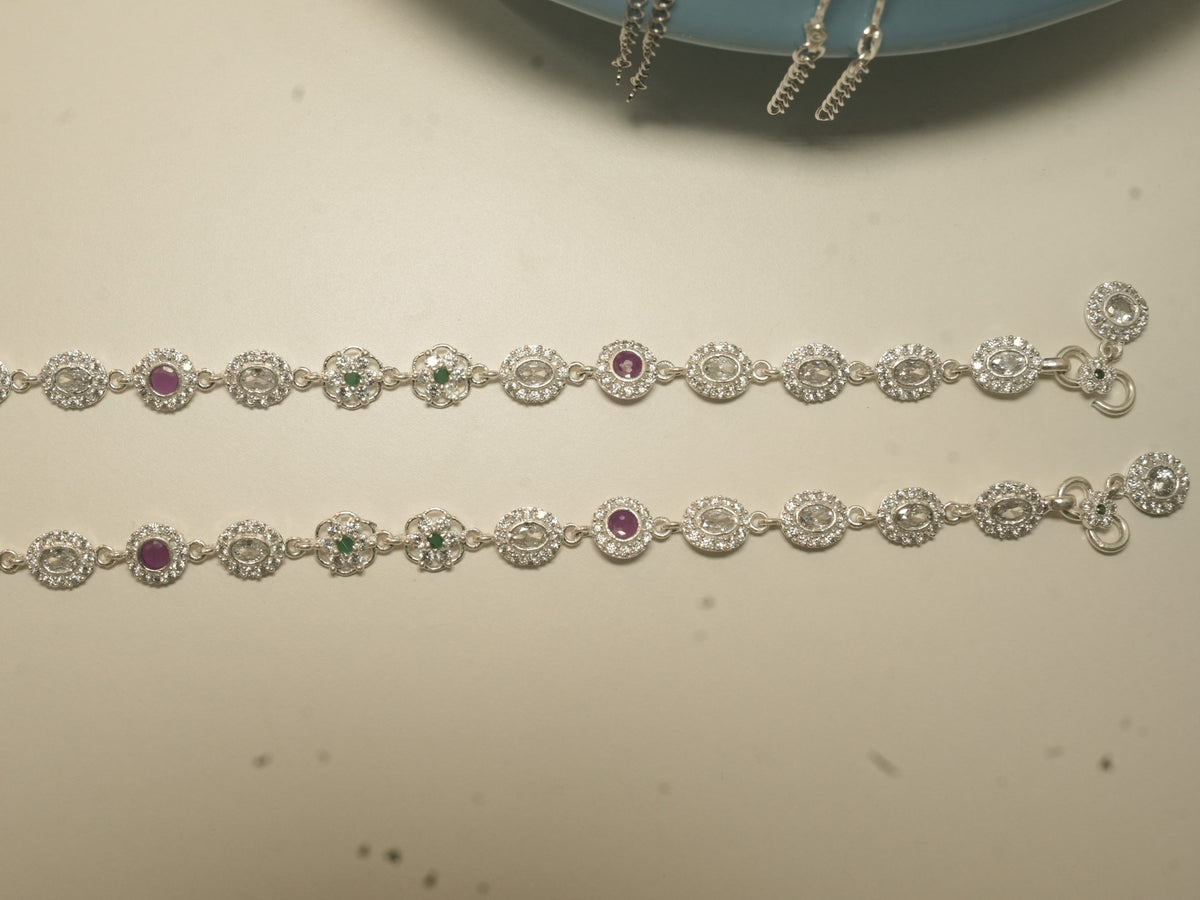 The pair of oval halo payal laid out full length, showing pink and green stone links among the colourless ones.